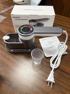 Portable handheld steam iron kit including measuring cup and instruction manual on desk