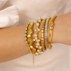 Stacked gold titanium bangles with pearls and zircon stones on a female wrist