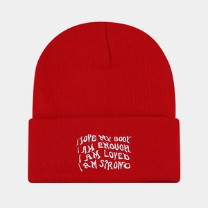 Detail of red knit beanie with white embroidered motivational quotes on the folded cuff