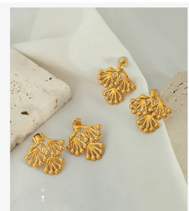 Macro view of golden pine branch stud earrings on elegant white textured stone