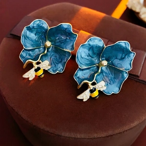 Vintage blue enamel flower stud earrings with detailed gold bee accent on a velvet base