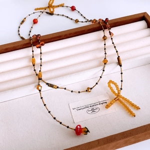Detail of vintage beaded necklace with amber glass beads and yellow bow pendant in a box