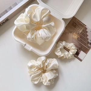 Close-up of three cream oversized satin scrunchies in varied sizes on a white surface
