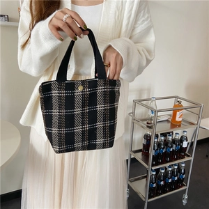 Close-up of retro plaid wool handbag featuring black handles and a gold button detail