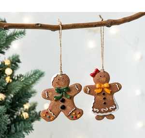 Detail of gingerbread man and woman ornaments hanging on a rustic branch with warm lights