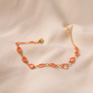 Detail of adjustable gold-plated chain bracelet with orange enamel charms on linen background