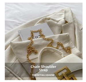 Detail of white leather crossbody bag with chunky gold chain strap and geometric metal buckle
