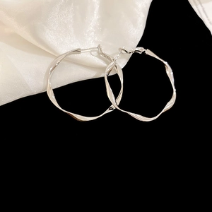 Close-up of irregular twisted silver hoop earrings on elegant white silk fabric