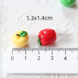 Macro shot of yellow and red resin apple charms measuring 1.3x1.4cm next to a white ruler
