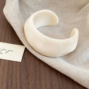 Close-up of wide cream acrylic resin cuff bracelet with a wrinkled geometric design on linen