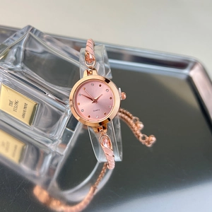 Detail of rose gold quartz watch with pink dial and crystal markers on glass stand