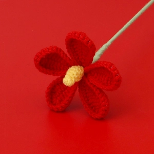 Detail of hand-crocheted red violet flower with yellow stamen and light green stem