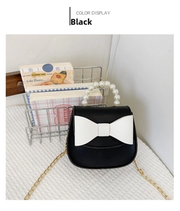 Detail of black mini crossbody bag featuring white bow, pearl handle and gold chain