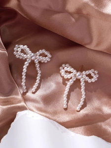 Detailed view of pearl bow earrings with tassels on elegant bronze silk background