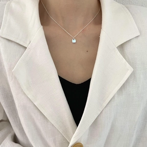 Macro view of light blue teardrop pendant necklace worn with a white linen blazer