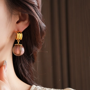 Detailed close-up of a model wearing gold irregular earrings with purple resin pendants