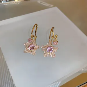 Macro detail of star-shaped earrings with pink center stone and gold hoop design
