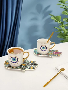 Macro shot of ceramic coffee cups with Hamsa hand saucer and golden spoon