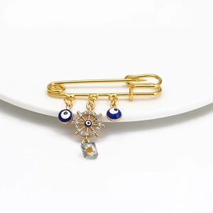 Detail of gold evil eye pin with blue enamel charms and a nautical wheel pendant