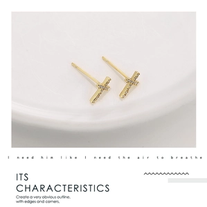 Close-up of gold T-shaped stud earrings with sparkling cubic zirconia on white ceramic
