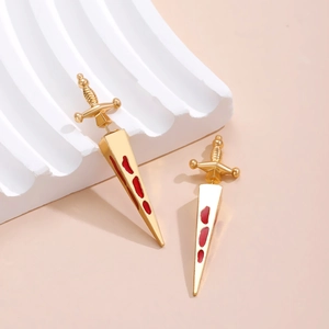 Detail of gold-tone dagger earrings with red drip oil effect on a wavy white base