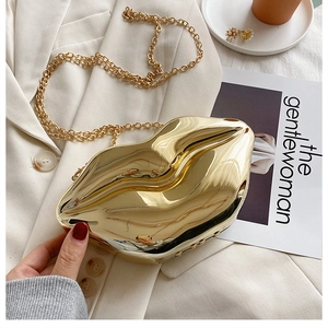 Detailed close-up of a gold lip-shaped clutch bag with chain on a white blazer background