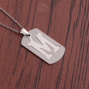 Collier en acier inoxydable argenté avec pendentif lettre M évidé sur fond marron structuré