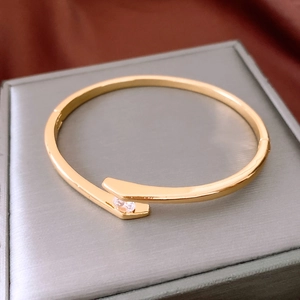 Macro detail of a gold-plated bypass bangle with zircon inlay on a velvet background