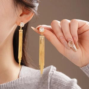 Close-up of sparkling cubic zirconia square studs and long gold tassel chains on ear