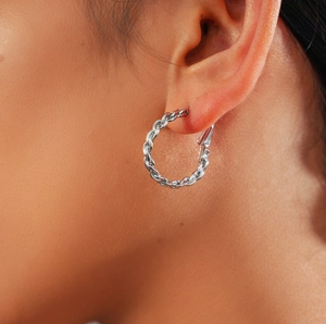 Détail d'une boucle d'oreille créole torsadée argentée portée sur un modèle chic