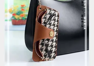 Detail of houndstooth glasses pouch with leather trim and gold flower clasp on a bag