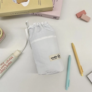 Close-up of white canvas drawstring stationery pouch with cute dog label and desk accessories