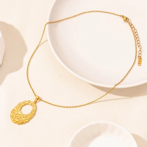 Retro 18k gold plated stainless steel hollow oval pendant necklace on a ceramic dish