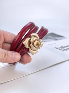 Detailed macro view of a red leather wrap bracelet with a golden metallic rose clasp buckle