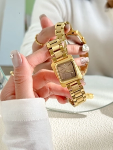 Détail d'une montre carrée dorée élégante avec cadran texturé et bracelet en métal