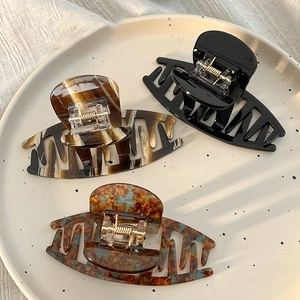 Three tortoiseshell acrylic hair claws in black, amber, and brown on a white plate