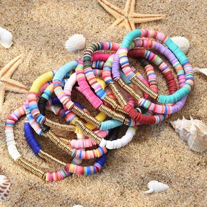 Detailed stack of colorful beach friendship bracelets with gold beads on ocean sand