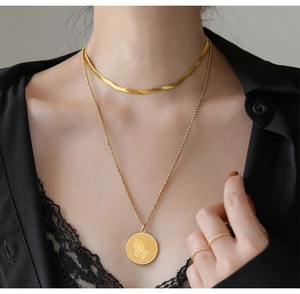 Detail of gold double-layered snake bone chain and round pendant with praying hands engraving