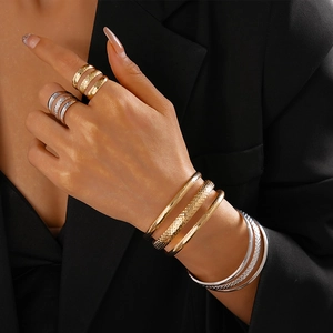 Layered gold and silver metal bracelets and rings set with hammered texture on model