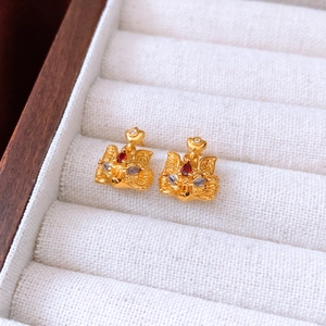 Macro detail of 24k gold-plated fox stud earrings with red crystal eyes on white velvet