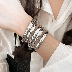 Close-up of five silver-finish bangles with hammered texture worn by a model