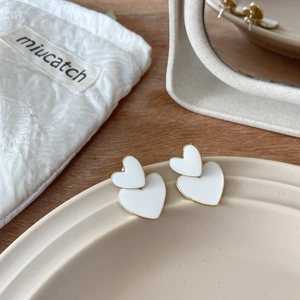 Detail view of heart-shaped white enamel earrings next to a branded fabric storage pouch