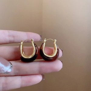 Close-up of U-shaped gold metal earrings with amber resin and tortoiseshell pattern