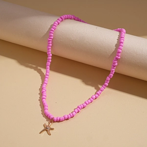 Detail of pink beaded necklace with gold starfish pendant on beige cylinder prop
