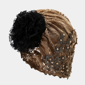 Détail d'un turban en dentelle marron avec grande fleur noire et broderies de perles