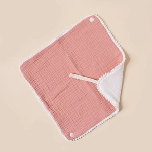 Detail of soft pink cotton baby bib showing pom-pom trim and snap button closure
