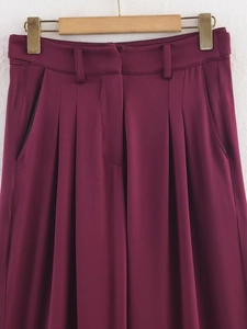 Detailansicht der weinroten plissierten Hose mit hohem Bund an einem Holzkleiderbügel