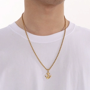 Detailed view of a gold anchor pendant necklace with rope chain worn on a male model neck