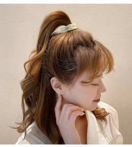 Detail of cream-colored claw clip securing a high ponytail on a model with hair accessory