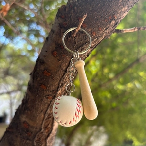 Mini baseball and wooden bat keychain hanging on a branch in natural outdoor light